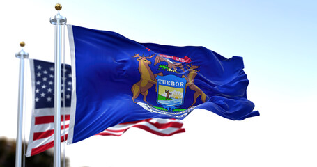 the flag of the US state of Michigan waving in the wind with the American flag blurred in the...