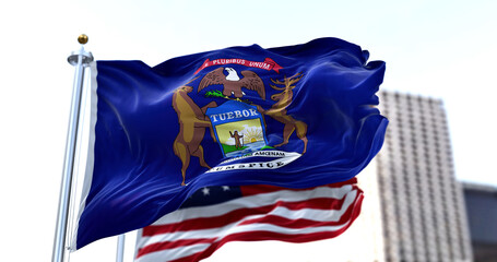 the flag of the US state of Michigan waving in the wind with the American flag blurred in the...