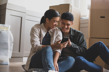 Mid adult couple sitting on the floor in new home using smartphone 