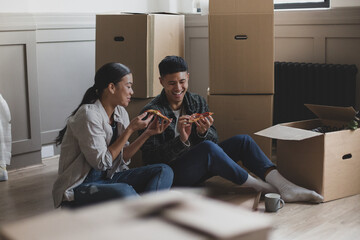 Mid adult couple sitting on the floor in new home eating pizza