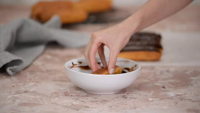 Hands dipping eclair in chocolate fondant.