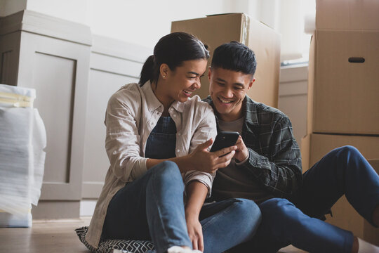 Mid adult couple sitting on the floor in new home using smartphone 