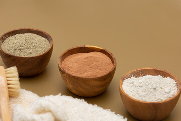 Organic green, red, white face mask clay in wooden bowls with soft sponge bandage and bamboo and goat hair brush on beige background. Home skin care concept.Self care
