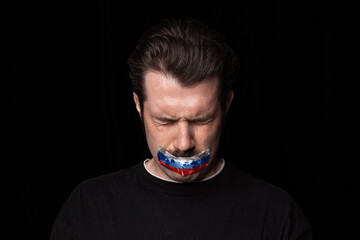 Conceptual portrait of young upset man with three colors duct tape over his mouth isolated on dark background. Censorship, freedom of speech concept.