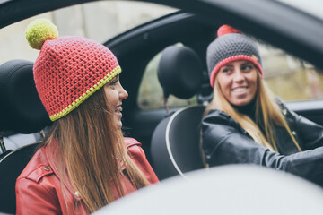 Trendy girls sitting in the car. Smiling teen in front of the steering wheel with a friend beside....