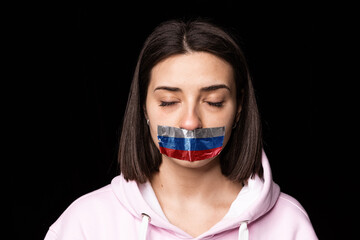 Portrait of young upset girl closed eyes and three colors duct tape over her mouth isolated on dark background. Censorship, freedom of speech concept.
