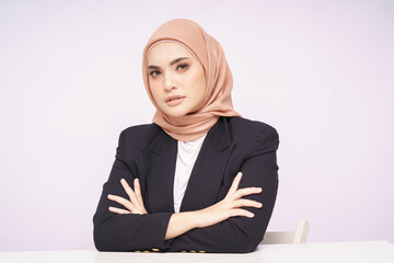 A beauty shot of a pretty young Asian hijab corporate girl with smooth glowing skin smiling and relaxing on a table over white background studio. Beauty skin care, office concept.