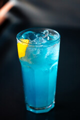 Glass of sweet cool blue cocktail with lemon and ice