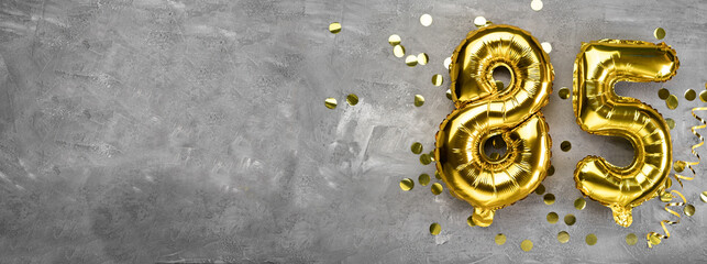 Yellow foil balloon number, number eighty-five on a concrete background. Greeting card with the...