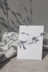 Blank paper card mock up, linen cloth and leaf shadows on surface.