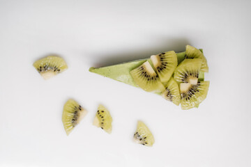 A piece of cake decorated with kiwi and pieces of fruit on the table.