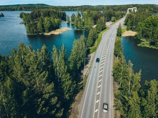Aerial view of road through blue lake and green woods in Finland.
