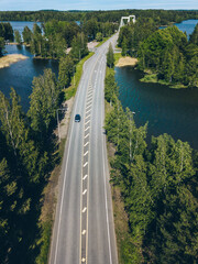 Aerial view of road through blue lake and green woods in Finland.