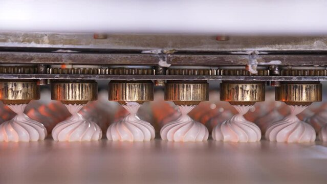 Metal nozzles are turning to squeeze creamy marshmallows on the conveyor belt. Confectionery production at food factory.