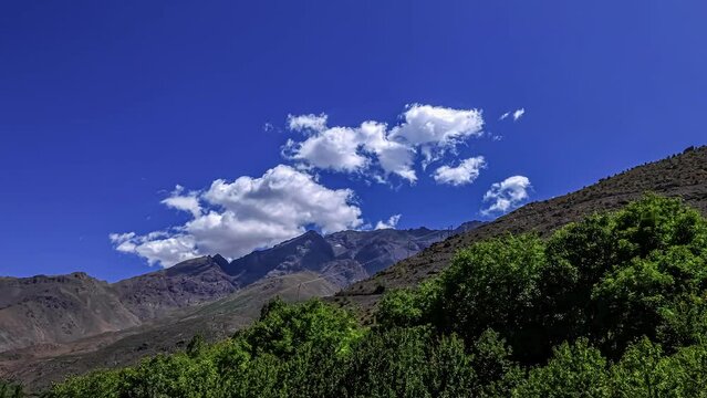 Hovering white clouds over massive Atlas Mountains during sunny day and blue sky in Africa - time lapse shot