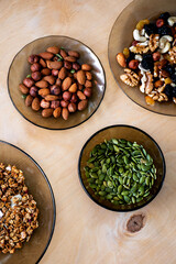 a plate of muesli bowl nuts raisin and beans green sunflower seeds, pumpkin seeds in the dishes and spoon on the light wooden background, healthy vegetarian food 