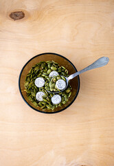 healthy breakfast a plate of pumpkin green seeds, nuts and in the dishes and spoon, white sweets candies, on the light wooden background towel, healthy vegetarian food 
