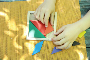Tangram logic toy, little boy hands assemble the puzzle
