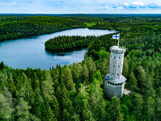 Aerial view of observation tower with Finnish flag among blue lakes and green forests in summer Finland.