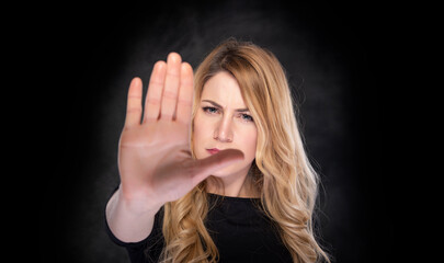 A woman points to a stop sign with her hand. On a dark background.