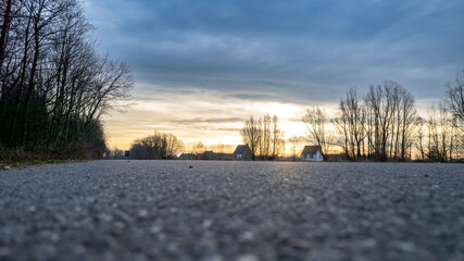 Obraz premium Low perspective vanishing point asphalt road between the trees of a forest under a dramatic and colorful sunrise or sunset sky. High quality photo