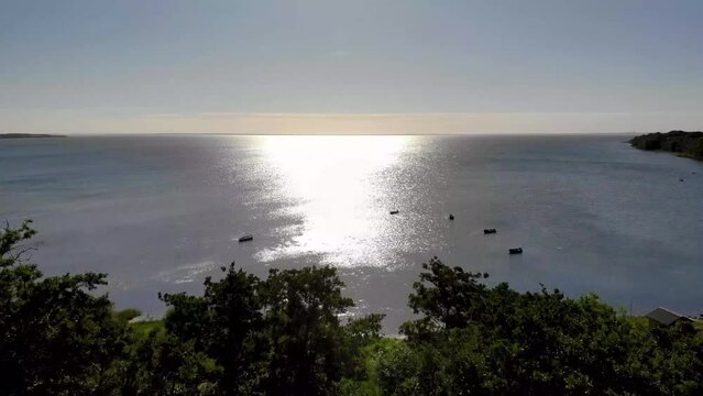 Aerial view flying across the sea in Nyk&oslash;bing Bugt over the woods towards the sun.
