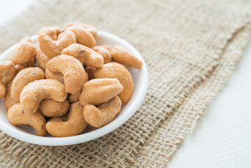 Salted cashew nuts in dessert bowl on sackcloth background. Food and nutrition concept.