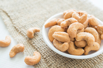 Salted cashew nuts in dessert bowl on sackcloth background. Food concept.