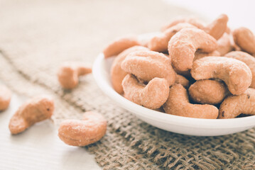 Salted cashew nuts in dessert bowl on sackcloth background. Food concept.