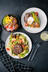 salad and bowl with juicy plant-based meat, avocado, egg, tomato, almond, greens, quinoa, radish, baby corn, quinoa, poached egg, cucumber and carrot. dark concrete background. top view
