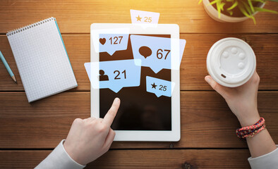 social media, technology and people concept - close up of female hands with virtual icons over tablet pc computer, notebook and coffee on wooden table