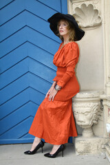 Attractive woman in an orange evening dress poses in front of a blue door