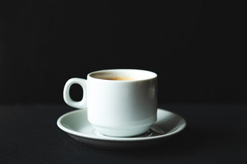 White cup of espresso coffee on a black background.