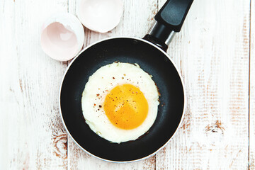 Fried egg in a frying pan on a wooden background.