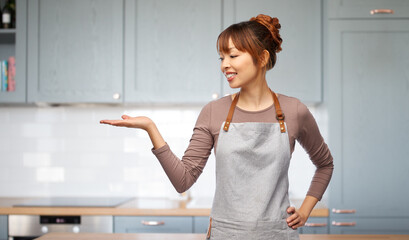 cooking, culinary and people concept - happy smiling woman in apron holding something imaginary on her hand over kitchen background