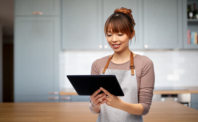 cooking, technology and people concept - happy smiling woman in apron with tablet pc computer over kitchen background