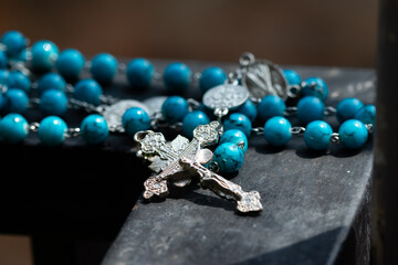 Rosary and cross made of blue stone beads on an iron fence.