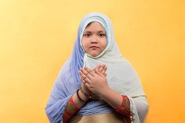 A religious Asian Muslim child girl in the Muslim hijab dress is praying to Allah or God during the Ramadan period