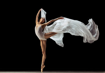 Graceful classic ballerina dancing with weightless fabric isolated on black studio background in neon. Theater, art, beauty, grace, action and motion concept.