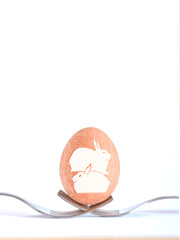 Easter background with an egg decorated by hand with drawings of white rabbits supported by two forks.