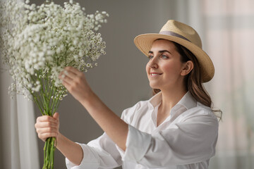 people, gardening and floral design concept - happy smiling woman or floral artist in straw hat holding bunch of gypsophila flowers at studio