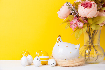 Easter eggs, ceramic chicken and a bouquet of flowers on a yellow background. Happy easter concept.