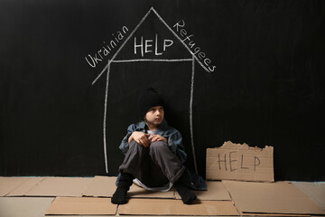 Homeless little girl sitting on floor near dark wall with drawn house. Help Ukrainian refugees