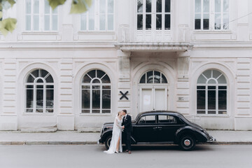 Wedding of a beautiful, stylish couple, a bride in a white wedding dress and a groom in a black suit, tuxedo, in a black retro car.
