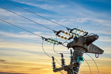 Concrete electrical pole with glass insulators on electrical cables, over yellow and blue sky at...