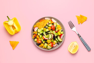 Fototapeta na wymiar Plate with Mexican vegetable salad, nachos, bell pepper and lemon on pink background