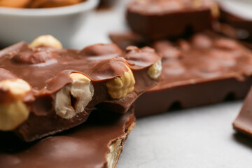 Pieces of tasty chocolate with hazelnuts on table, closeup