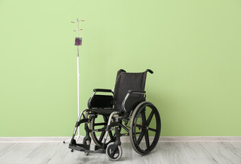 Fototapeta na wymiar Empty wheelchair and stand for IV drip near color wall