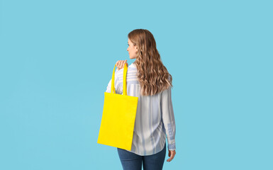 Pretty young woman with yellow eco bag on blue background