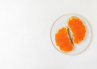 2 toasts with red caviar and cream cheese on a plate on a white background, top view